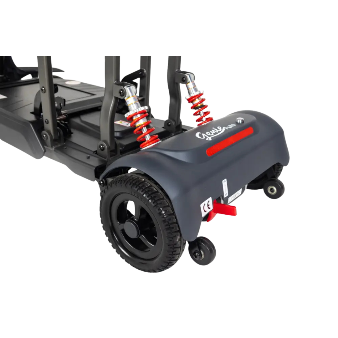 Close-up view of the rear wheels and suspension system of the Monarch Genie Auto Folding Portable Scooter, featuring red shock absorbers, black tires, and branding on its dark blue body.