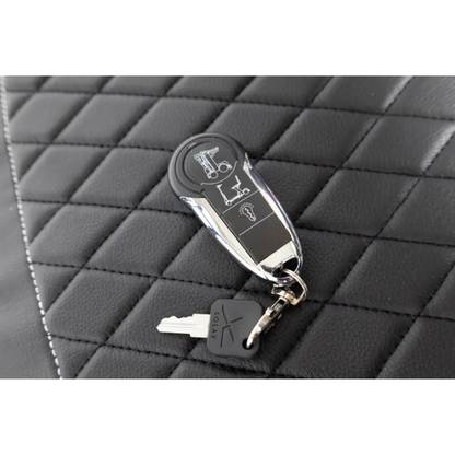 A close-up of a Monarch Genie Auto Folding Portable Scooter key fob and standard key with a black plastic head, resting on black, diamond-stitched leather upholstery.