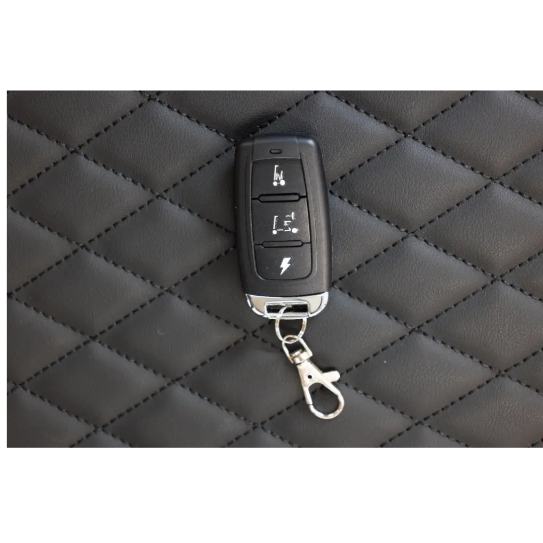 A Monarch Smarti Plus Ultra-Lite Auto Folding Scooter key fob with three buttons and a metal keychain clip rests on a quilted black leather surface.