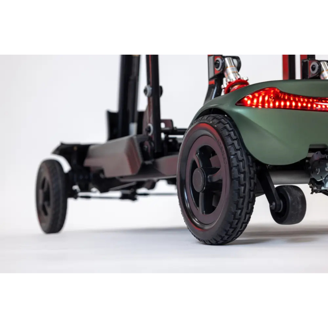 Close-up of the rear and side wheels of the Monarch Smarti Plus Ultra-Lite Auto Folding Scooter, featuring a green frame, red LED light, and black tires on a white background.
