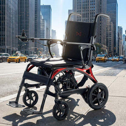 A Monarch Ezi Fold Carbon Portable Power Wheelchair with black and red accents is parked on a city sidewalk amid tall buildings, yellow taxis, and sunlight in the background.
