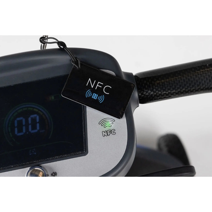 Close-up of the Monarch Supa Carbon Lite Ultra-Lightweight Carbon-Fiber Scooter dashboard with digital display showing 0.0 and an NFC symbol. A black NFC key tag hangs by the handlebar, highlighting secure, contactless access for users.