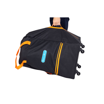 A person holds a Rolling Travel Bag for Monarch Mobility Portable Scooters—large, black, with orange handles and zippers, and a blue-and-white logo patch. The folding bag is slightly tilted and lifted off the ground.
