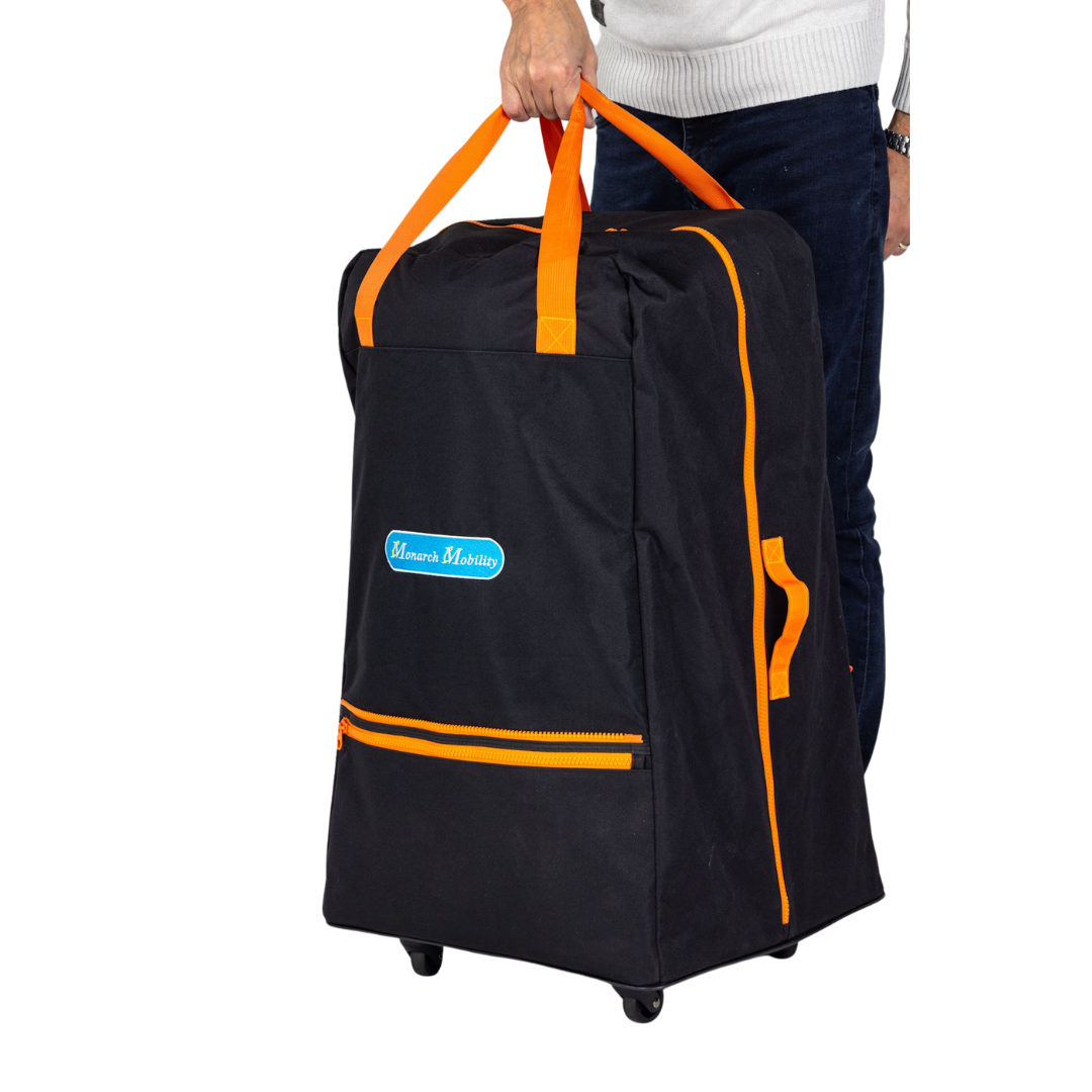 A person in a white sweater and jeans holds an upright Rolling Travel Bag for Monarch Mobility Portable Scooters with orange handles, front zipper pocket, “Mamas Marisha” logo, and wheels.