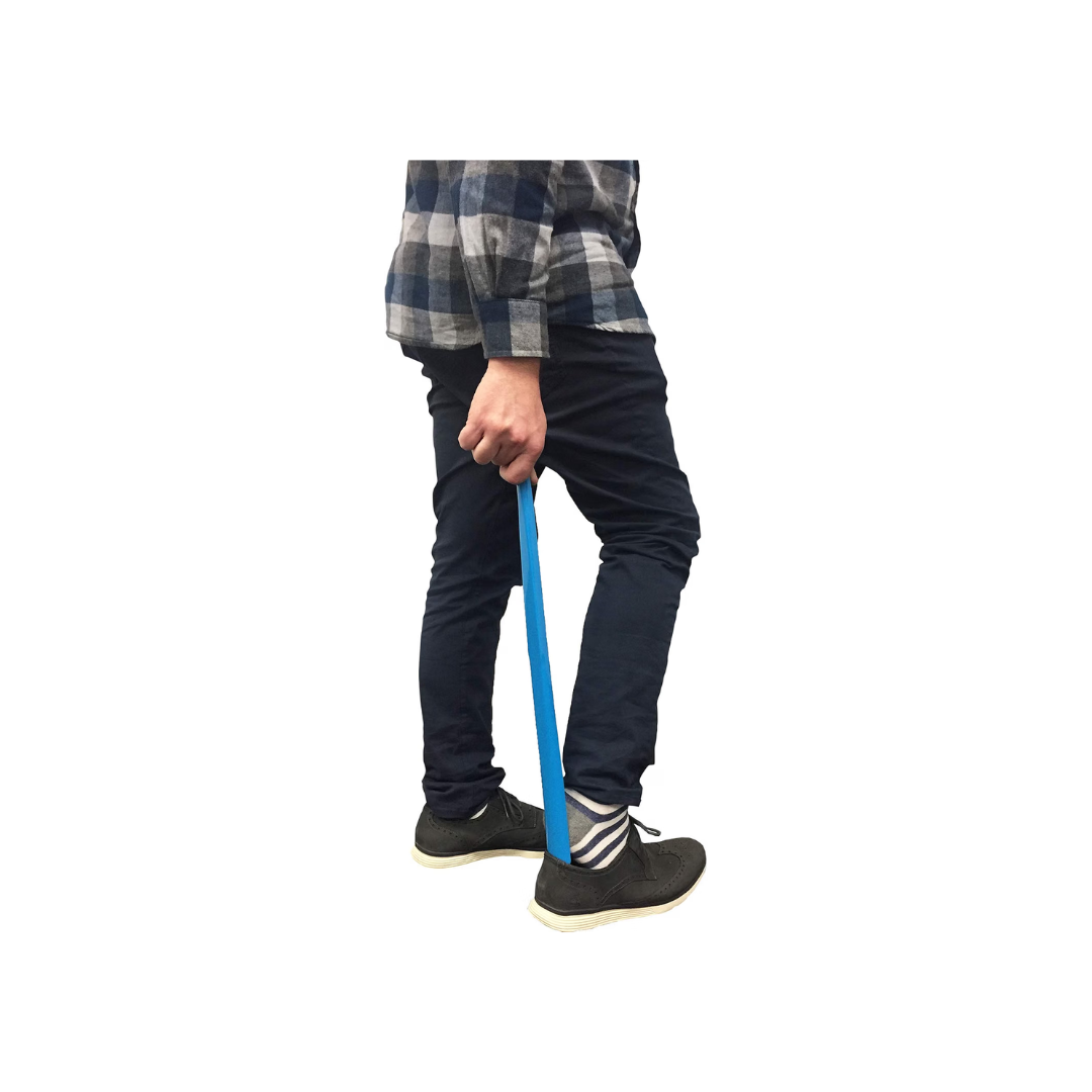 A person uses the Nova 24″ Extra Long Shoe Horn from the Pack of 2 to comfortably slip on black shoes. Wearing dark pants, a plaid shirt, and striped socks, they find it effortless to put on their shoes thanks to the extra-long design of the blue shoe horn.