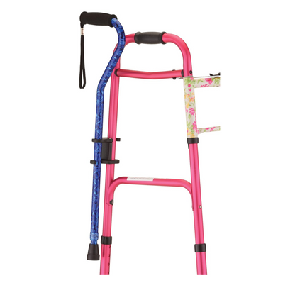 The NOVA Medical Cane Holder for Rollators and Folding Walkers, shown with a pink walker and blue cane, features a floral-patterned clamp to securely hold the cane; both stand upright against a white background.