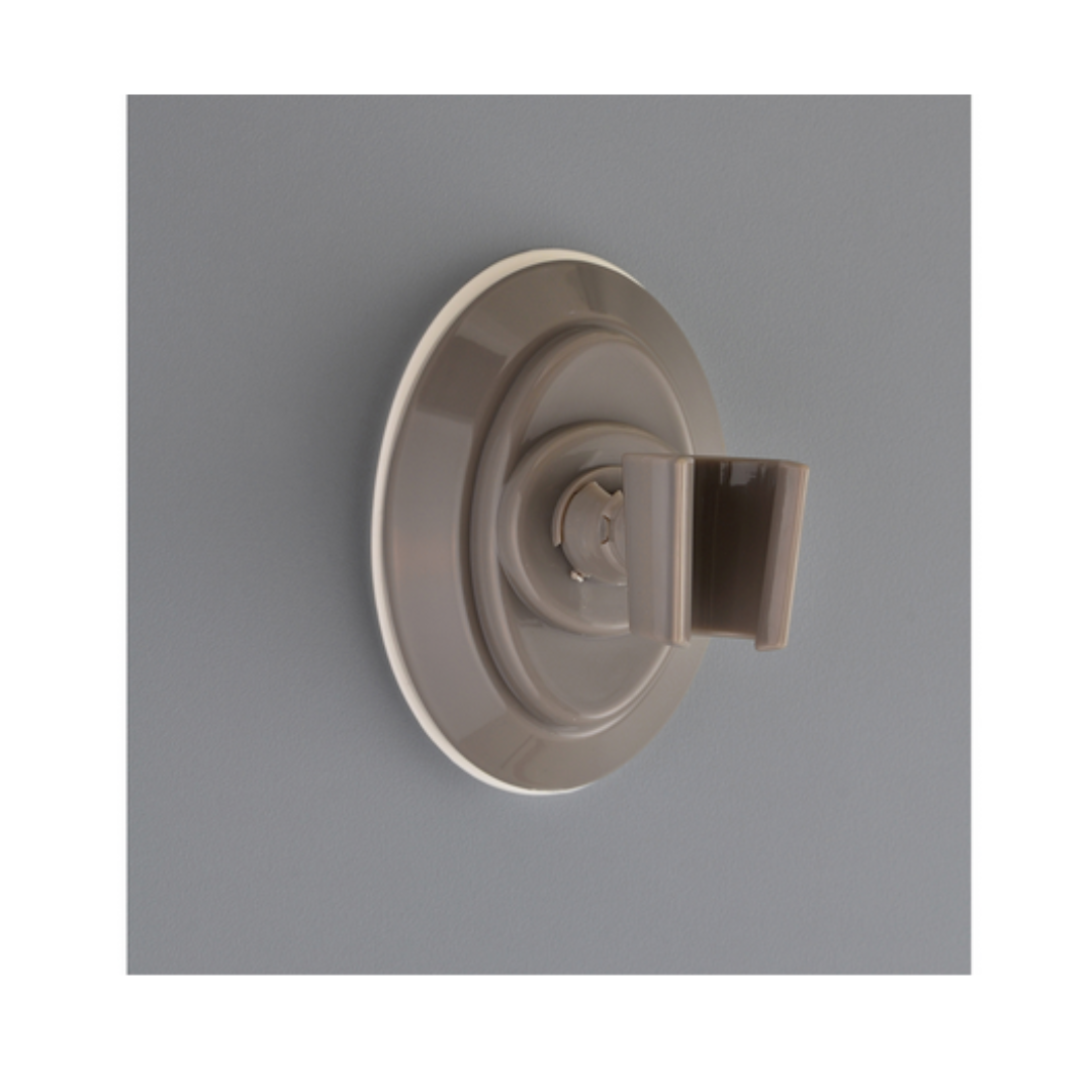 The Nova Suction Cup Showerhead Holder in gray is attached to a smooth, light gray wall with its removable suction cup holder.