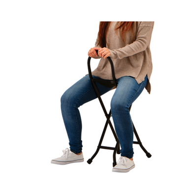 A person sits on the Nova 3092 Folding Travel Seat Cane With Sling Seat, holding its handle. Dressed in a beige sweater, blue jeans, and white sneakers, they highlight the unique curved frame of this portable walking cane against a white background.