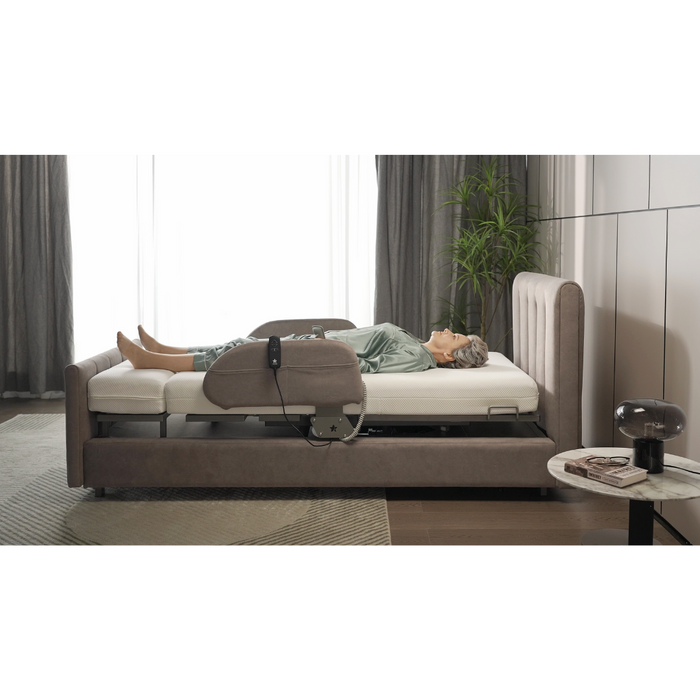 Lounging in pajamas on the Starsleep Orin Rotating Full Electric Lift Assist Bed with Heat & Massage, a person enjoys its multifunctional design and raised backrest in a room with neutral tones, a potted plant by the window, gray curtains, and a small round table topped with a lamp.