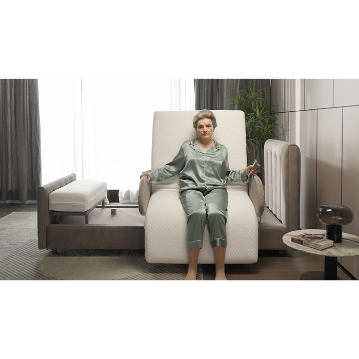 In a softly lit modern room with gray curtains, a person in silk pajamas sits on the Starsleep Orin Rotating Full Electric Lift Assist Bed with Heat & Massage set in a comfortable semi-upright position, surrounded by a plant and small side table.