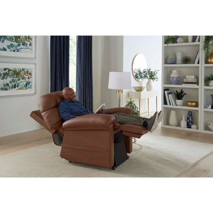 A person relaxes in a Golden Tech PR515 Cloud Recliner With Lift Assist, ZG+ & Twilight - SM/MD, reading a book in a modern living room with a light rug, round mirror, and decorative items on white shelves. Blue curtains frame large windows for ergonomic support and ultimate comfort.