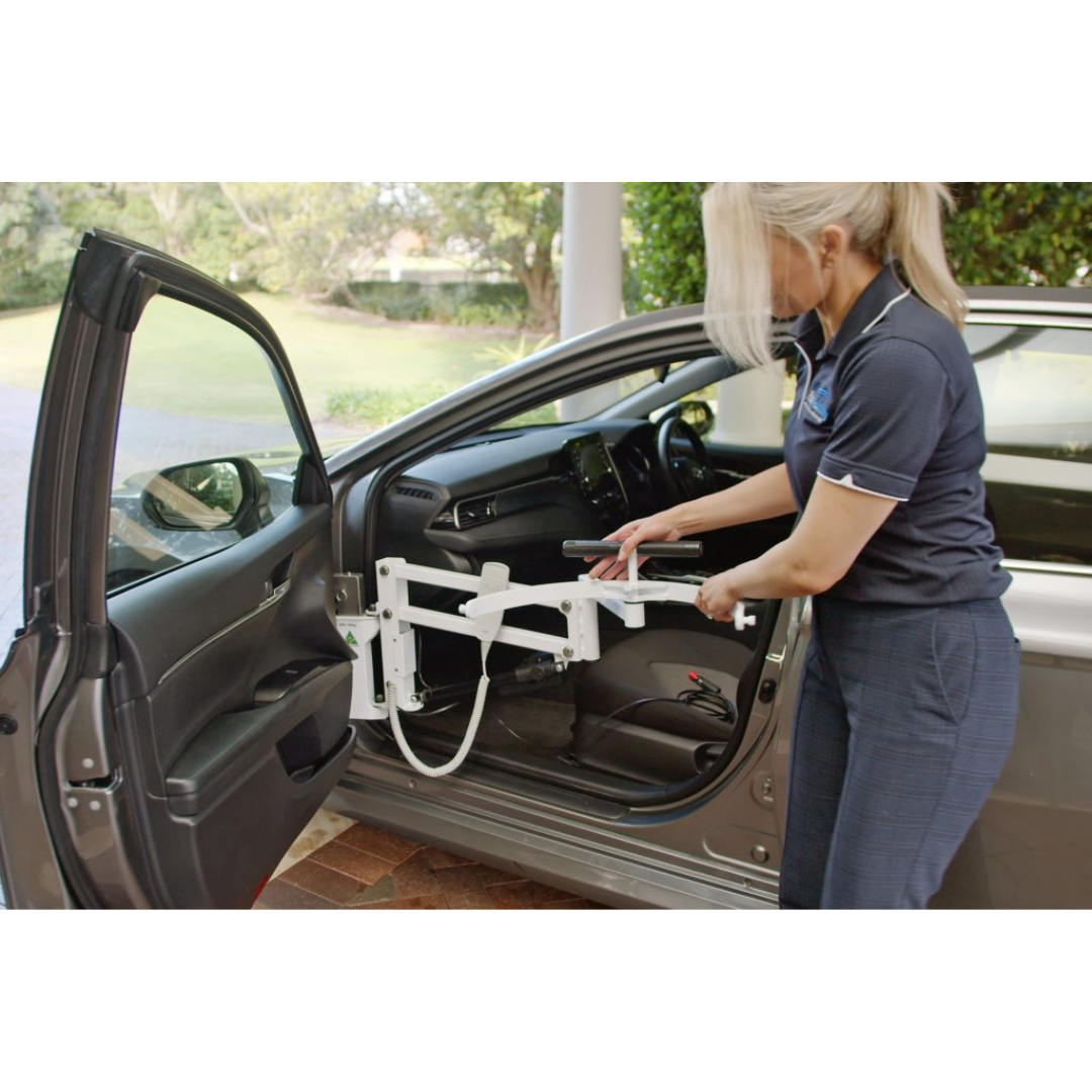 A woman stands beside an open car door, adjusting the Para Mobility IBIS Wheelchair to Car Access Lift, a transfer aid designed to help individuals with disabilities enter or exit the vehicle.