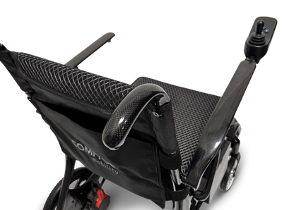 Close-up of the sleek black ComfyGo Phoenix Carbon Fiber Electric Wheelchair, showcasing its fabric seat and backrest. With armrests and a right-side joystick control, it features foldable carbon fiber spokes and displays the COMFY mobility label on the backrest.