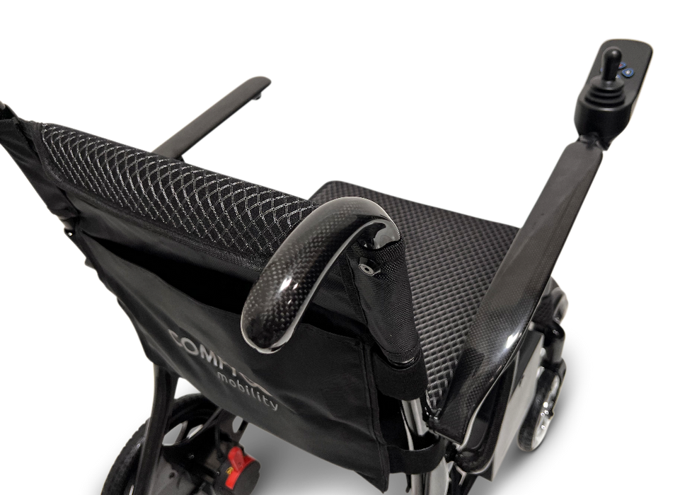 Close-up of the sleek black ComfyGo Phoenix Carbon Fiber Electric Wheelchair, showcasing its fabric seat and backrest. With armrests and a right-side joystick control, it features foldable carbon fiber spokes and displays the COMFY mobility label on the backrest.