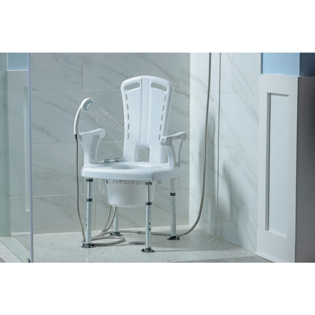 The Drive PreserveTech™ Aquachair Bathing System with Bidet, a white non-slip shower chair with armrests and adjustable legs, is placed in a tiled shower with water from a handheld showerhead spraying onto it and its removable bucket set beneath the seat.