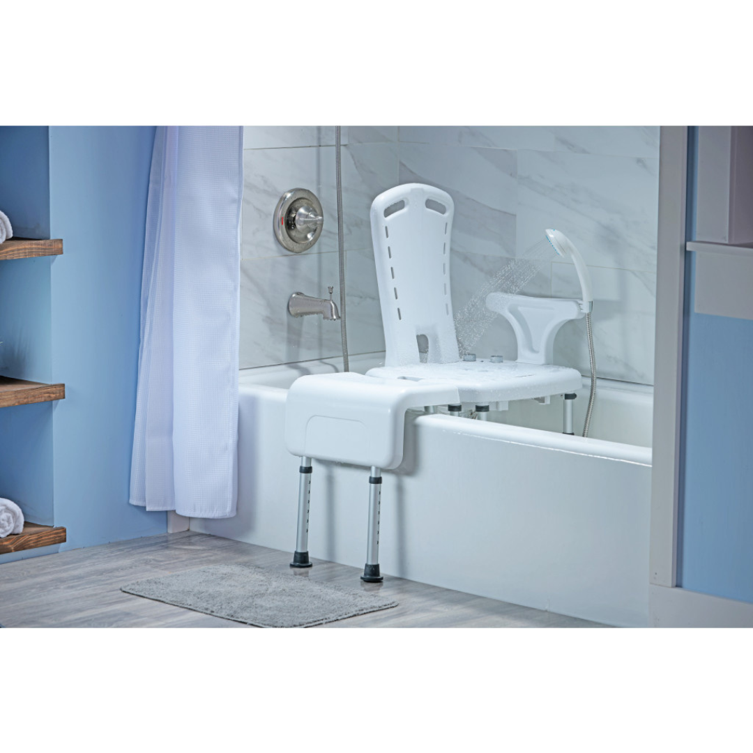 The bathroom features light blue walls, a gray bath mat, shelves with rolled towels, and the Drive PreserveTech™ Aquachair Bathing System with Bidet—a white shower chair with adjustable legs for independent bathing across the tub.