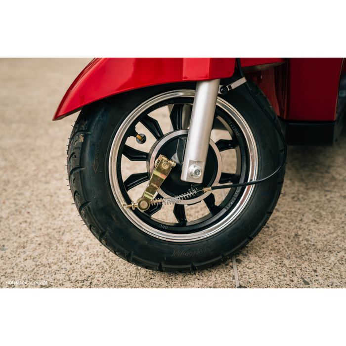 Close-up of a black tire and silver wheel on a red Pride Baja® Raptor® 2 Bariatric 3-Wheel Scooter, highlighting full suspension and brake components as the mobility scooter is parked on a concrete surface.