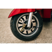 Close-up of a black tire and silver wheel on a red Pride Baja® Raptor® 2 Bariatric 3-Wheel Scooter, highlighting full suspension and brake components as the mobility scooter is parked on a concrete surface.