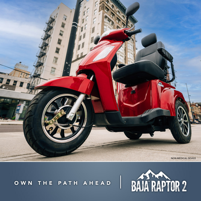 A vibrant red Pride Baja® Raptor® 2 Bariatric 3-Wheel Scooter with LED lights is parked on a city sidewalk amid tall buildings. The image displays the text: Own the Path Ahead | Baja Raptor 2.