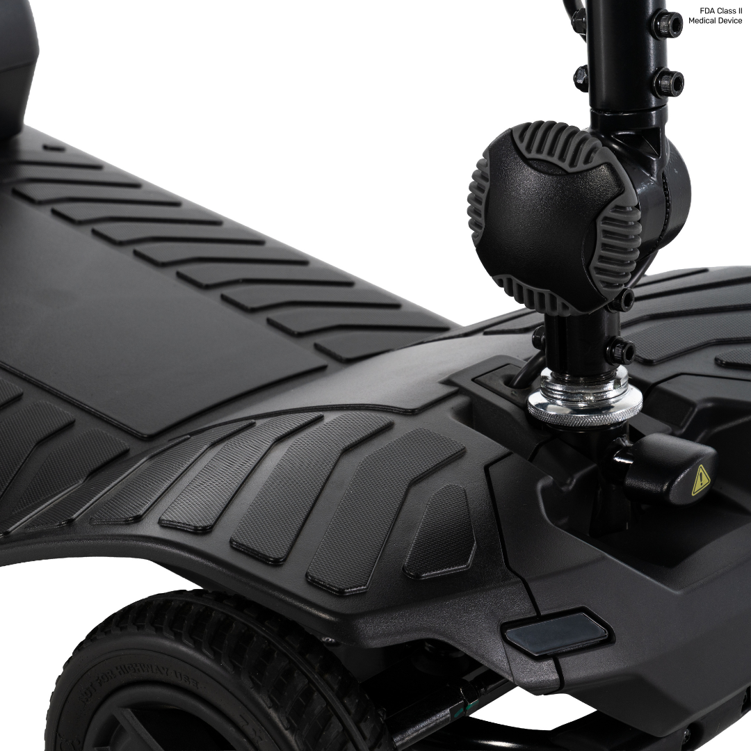 Close-up of a black Pride Go Go® Ultra X Gen 3 Portable Mobility Scooter’s textured footrest and front wheel area, showcasing detailed tread patterns and a section of the steering column. This portable scooter exemplifies both functionality and carefully considered design in every detail.