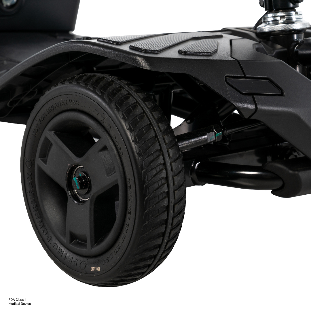 Close-up of a black, textured wheel attached to a Pride Go Go® Ultra X Gen 3 Portable Mobility Scooter, highlighting the tread details and a section of the scooter’s black frame against a white background.