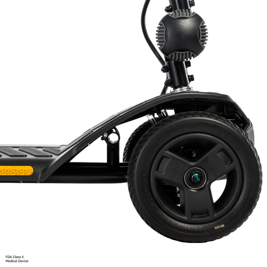 Close-up of the front wheel and deck of a Pride Go Go® Ultra X Gen 3 Portable Mobility Scooter in black, showing the tire, part of the frame, and a yellow reflector on the side.