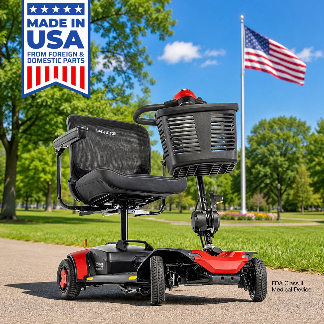 A red Pride Go Go® Elite Traveller Gen 3 Platinum portable mobility scooter with a black seat and front basket sits on a park path near an American flag.