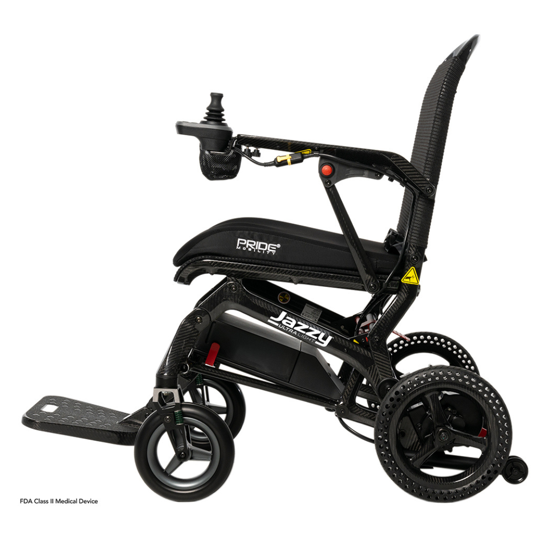 Side view of a black Pride Mobility Jazzy® Ultra Light Portable Electric Wheelchair featuring a cushioned seat, armrests, right-arm joystick, foldable design with footrest. The compact build has an ultra-light frame for easy transport and storage.