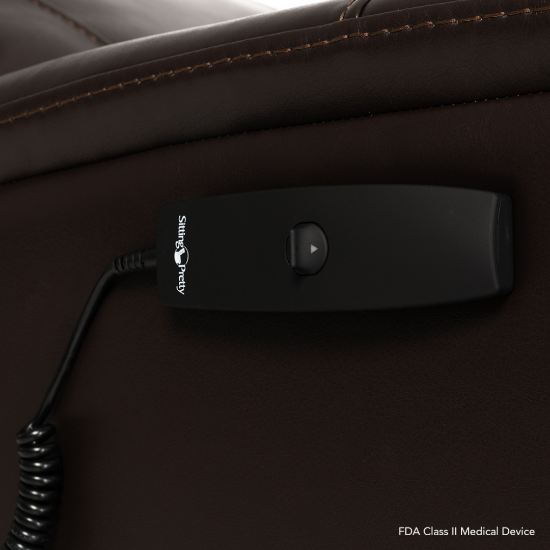 A black wired remote with a single button rests on dark brown leather. It features the Sitting Pretty logo and is attached by a coiled cable to the Pride Mobility Genesis LC150 Lift Chair Recliner—see product specs for details.