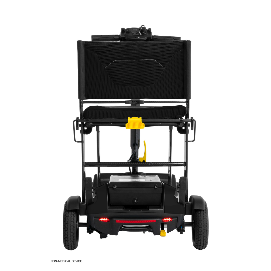 Rear view of a black Pride Mobility Go Go® Super Portable Mobility Scooter with foldable seatback, small wheels, and a yellow lever beneath the seat. This scooter has a compact design, lightweight frame, airline-approved battery, and non-medical device label on the bottom left.
