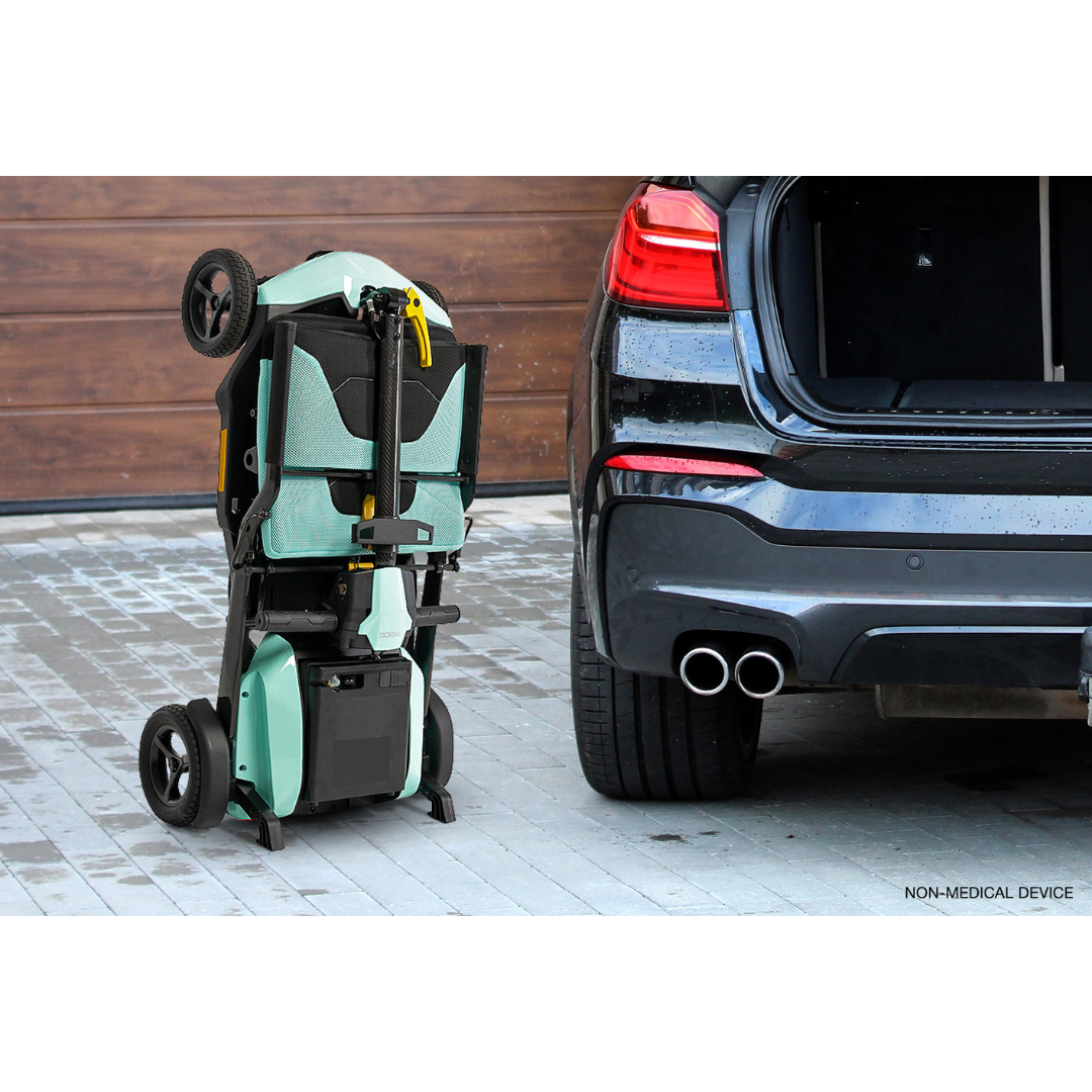 A folded wheelchair with large black wheels and a teal seat stands upright next to an open car trunk, highlighting its compact design alongside the Pride Mobility Go Go® Super Portable Mobility Scooter, set against the warmth of a wooden garage door.