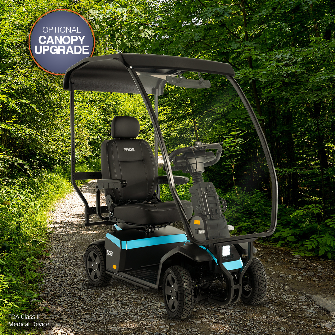 A Pride Mobility PX4 HD Bariatric Scooter, labeled FDA Class II Medical Device with a canopy upgrade, sits on a wooded dirt path in dappled sunlight beneath green trees. The black and blue scooter stands out in the forest setting.