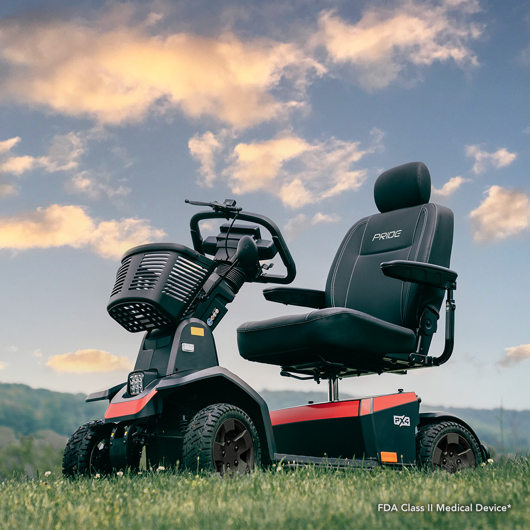 A Pride Mobility PX4 HD Bariatric Scooter, featuring four wheels, a black seat, and armrests, is pictured outdoors on grass beneath a partly cloudy sky with hills in the background.