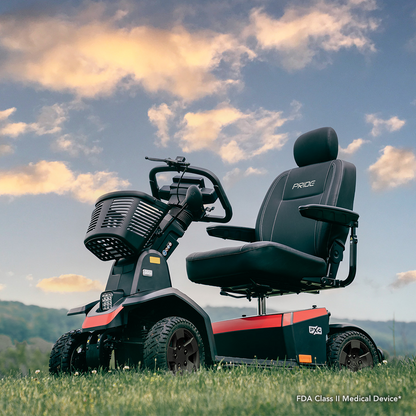 A Pride Mobility PX4 HD Bariatric Scooter, featuring four wheels, a black seat, and armrests, is pictured outdoors on grass beneath a partly cloudy sky with hills in the background.