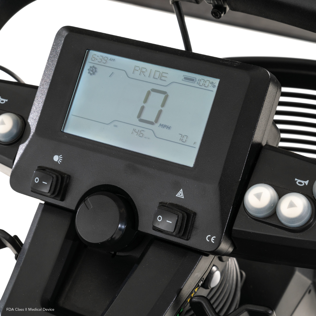 Close-up of the Pride Mobility PX4 HD Bariatric Scooter’s digital dashboard showing 0 mph speed, 100% battery, 6:39 AM time, and PRIDE. The panel includes buttons and indicator symbols on both sides.