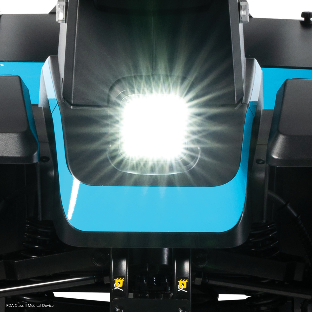 Close-up of the bright white headlight on a blue and black Pride Mobility PX4 HD Bariatric Scooter, with radiant light flares visible from the center.