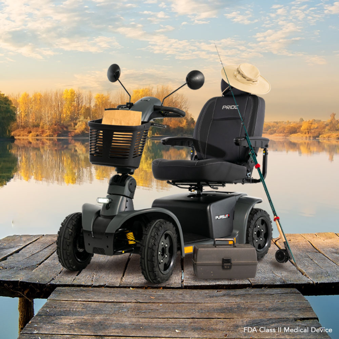 The Pride Mobility Pursuit® 2 Offroad HD Scooter, equipped with a basket, fishing rod, and fishing box, rests on a wooden dock by a calm lake with vibrant autumn trees—a great choice for lakeside adventures.