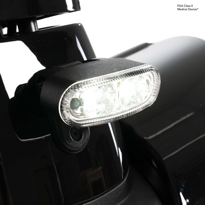 Close-up of a bright LED headlight on the glossy black Pride Mobility Pursuit® 2 Offroad HD Scooter, with an FDA Class II Medical Device label visible in the top right corner.