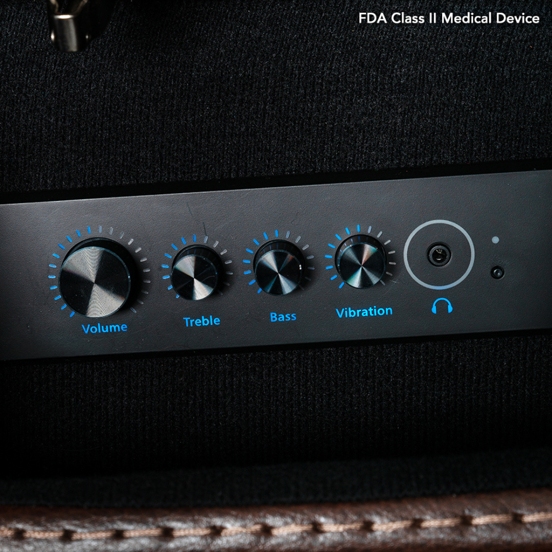Close-up of the black control panel on the Pride VivaLift! Premier Recliner With Assisted Lift, Audio & Massage. Blue-lit dials labeled Volume, Treble, Bass, Vibration, and a headphone jack. FDA Class II Medical Device text is shown.