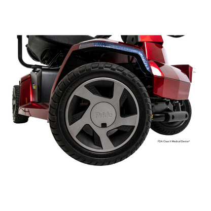 Close-up of the rear wheel and frame of a red Pride Mobility Zero Turn 10 HD Scooter, showing black treaded tires and detailing with the Pride logo on the hub. This midsize scooter features advanced EZ Turn Technology for tight maneuvering.