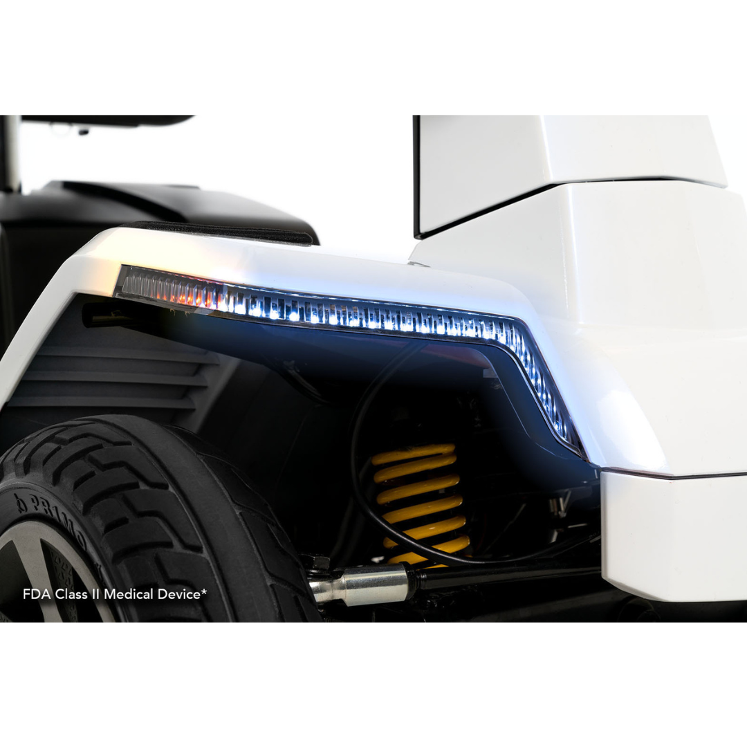 Close-up of the Pride Mobility Zero Turn 10 HD Scooter’s front wheel area, showing EZ Turn Technology, an LED light strip, large treaded tire, yellow suspension spring, and part of the white body. Text: FDA Class II Medical Device®.