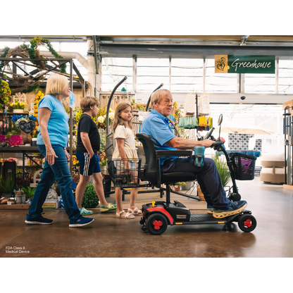 A man on a Pride Go Go® Elite Traveller Gen 3 Platinum Portable Scooter travels with a woman and two children through a greenhouse, as seen in these videos.