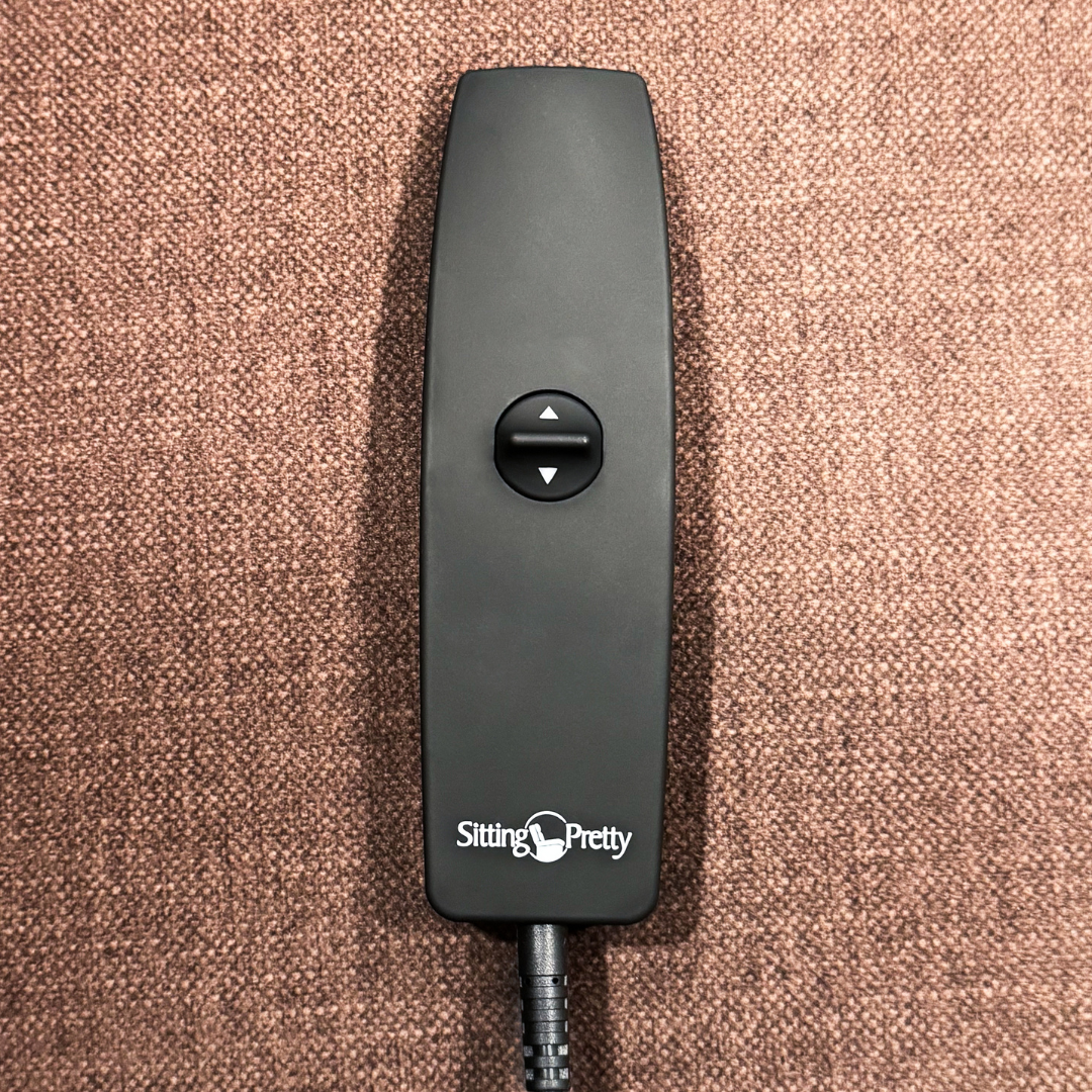 A black remote with up/down arrow buttons, labeled Sitting Pretty, rests on a textured brown surface—it belongs to the Pride Mobility Genesis LC150 Lift Chair Recliner; see product specs for more details.