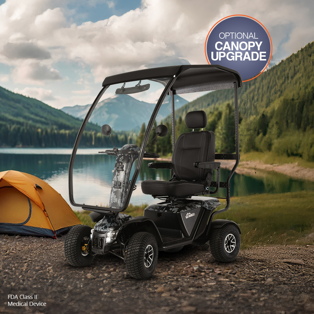 The Pride Baja® Wrangler® 2 Heavy Duty Outdoor Scooter with Canopy is parked on grass by a lake and mountains next to a yellow camping tent, under partly cloudy skies, highlighting its outstanding outdoor capabilities.