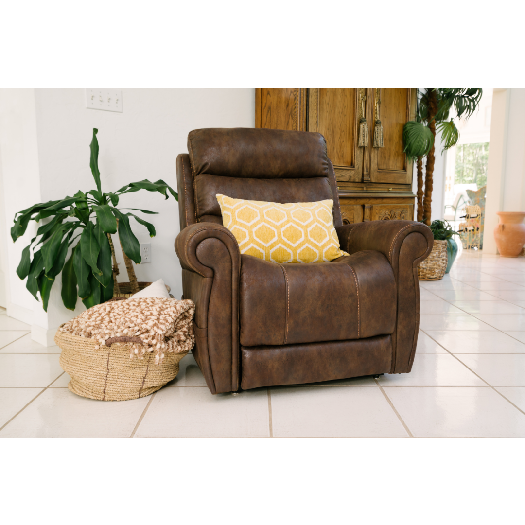 A Pride Mobility VivaLift!® Tranquil 2 Recliner with Lift Assist in brown leather, accented by a yellow patterned pillow, is placed near a green houseplant and a woven basket with a textured blanket in a bright, tiled room.