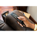 A person’s hand presses a button on the remote control of a brown leather Pride Mobility VivaLift! Radiance Recliner with Lift Assist & Heat, adjusting the chair’s infinite positioning and other settings.