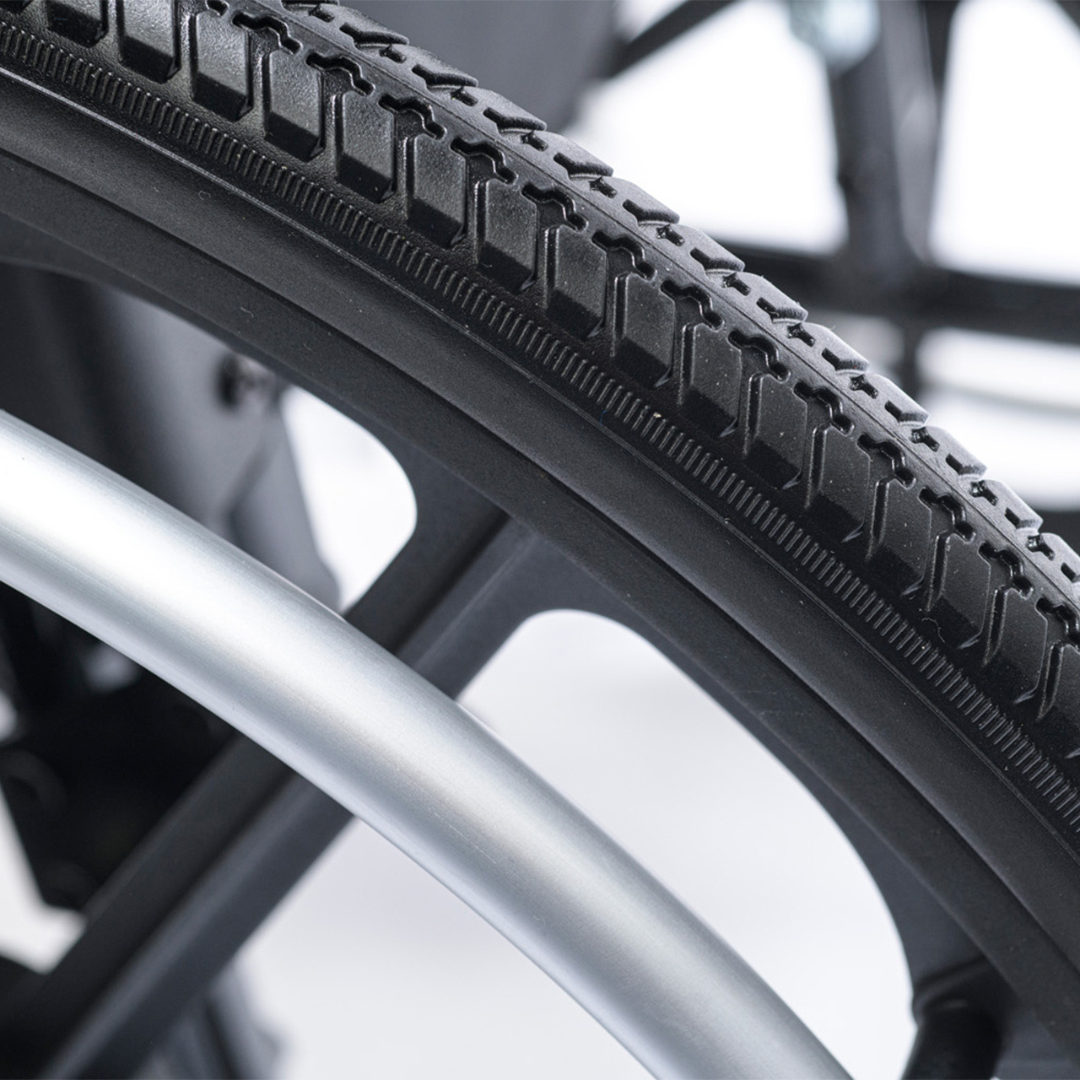 Close-up of a black rubber tire with textured tread beside a metallic silver rim, set against a blurred background—ideal for the Proactive Chariot IV XTC Pediatric Wheelchair, which features adjustable back height and lightweight design.