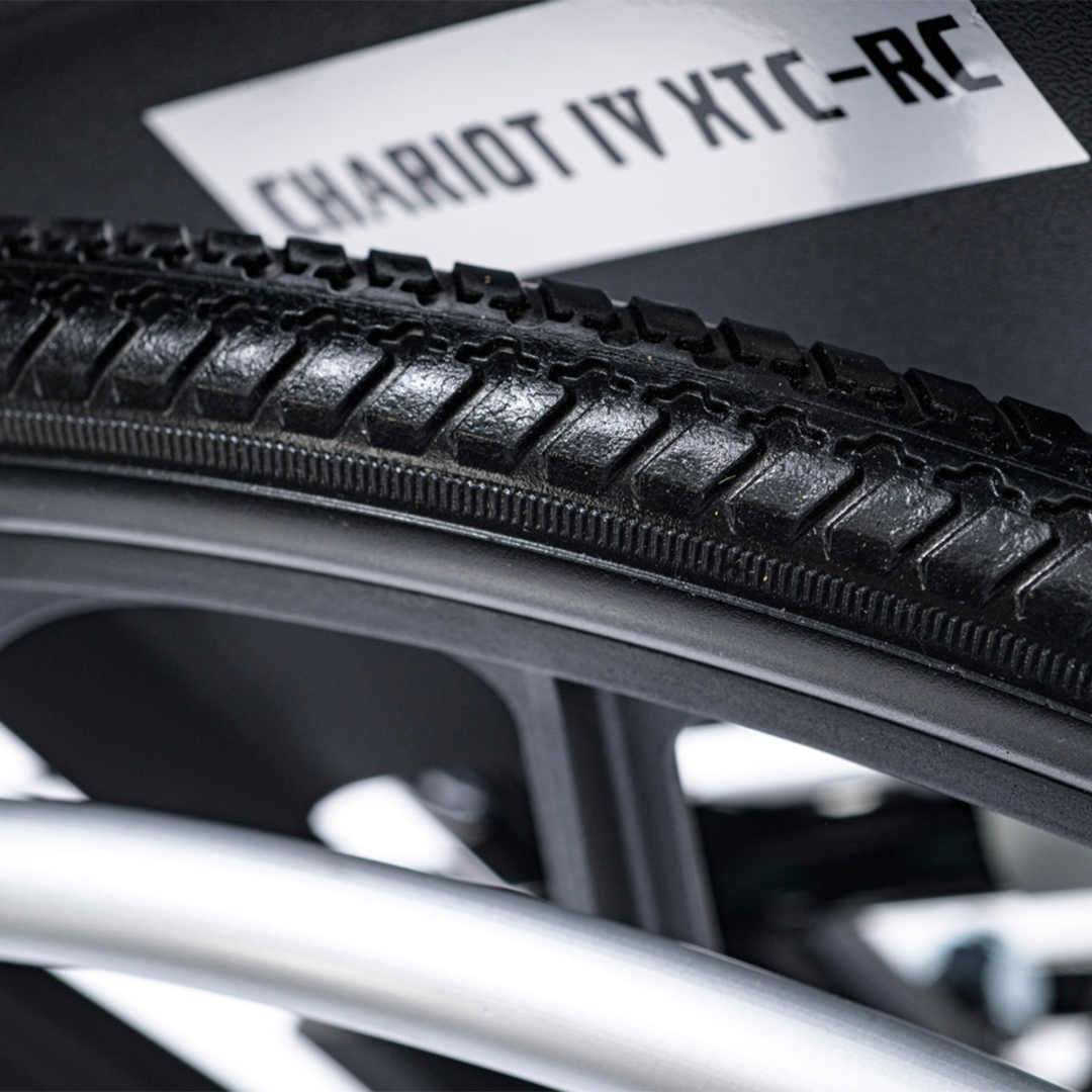 Close-up of a black, textured tire labeled Proactive Chariot IV XTC-RC on a pediatric folding reclining wheelchair with a durable carbon steel frame in the background.