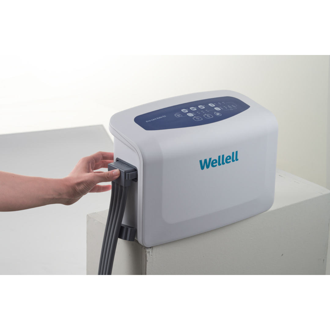 A person connects a hose to the Wellell Procare Auto G2 | Alternating Pressure & LAL Mattress System, featuring a digital control panel and placed on a white surface—an essential device for managing Low Air Loss and Alternating Pressure Mattresses.