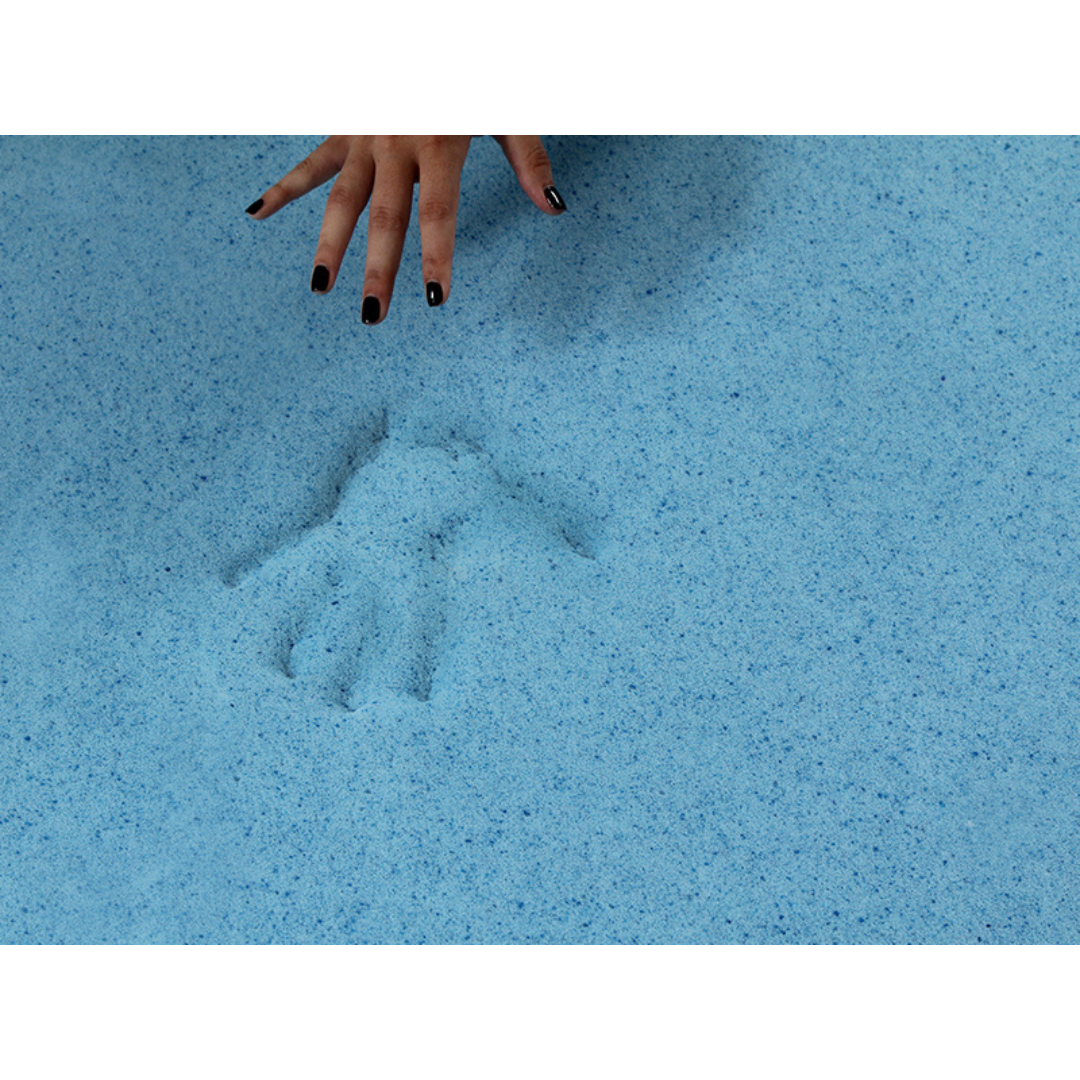 A hand with black-painted nails hovers above light blue sand, leaving a clear handprint—showcasing the soothing, pressure-relieving comfort of the Protekt® Ultra Molded Dual-Layer Portable Mobility Cushion.